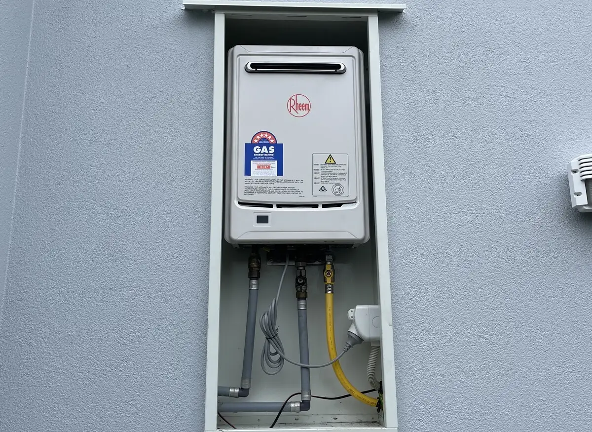 Rheem continuous flow gas water heater with its gas energy rating label, mounted in a weather box on a grey exterior wall