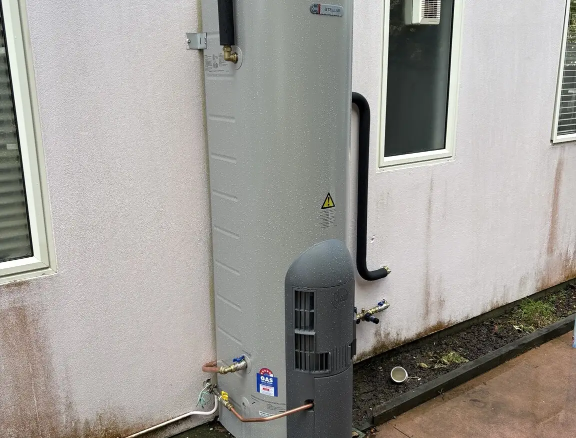 Outdoor hot water cylinder installed on a concrete pad against the wall of a house