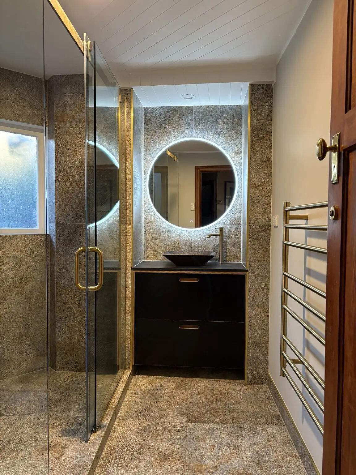 Finished dark-tiled bathroom renovation with brass tapware