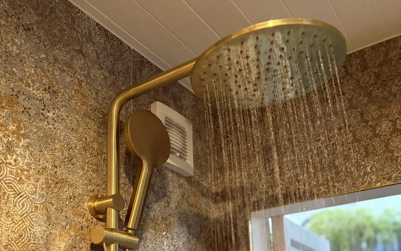 Brushed brass rain shower with a matching handset, running at full flow