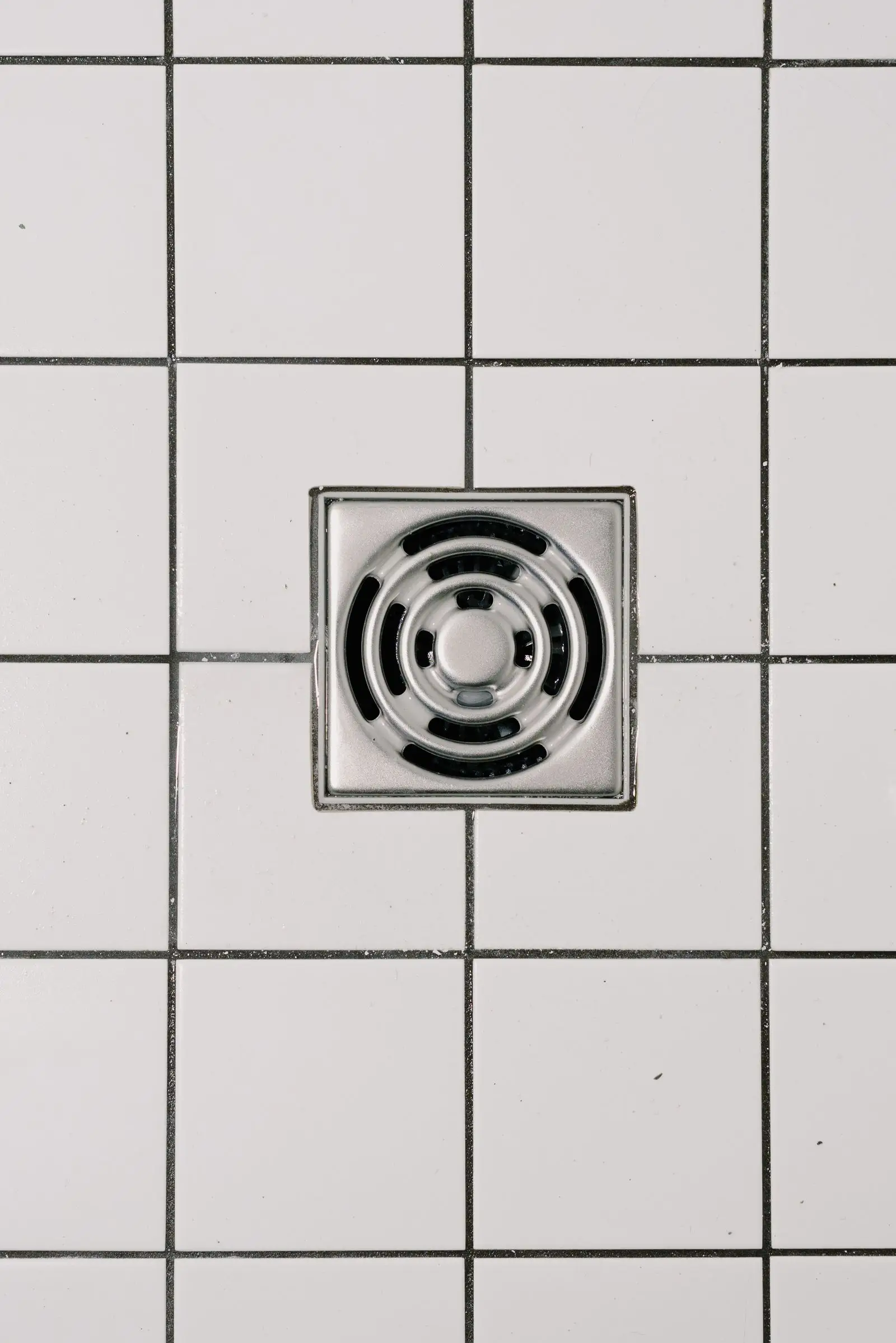 Square shower floor waste on a white tiled floor